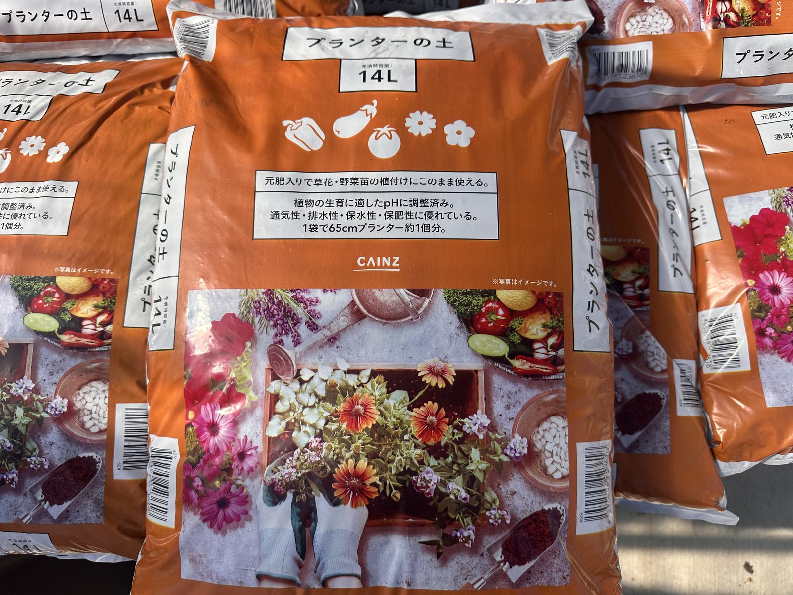 カインズの店頭に並ぶオレンジの袋の「プランターの土」14L。表に「1袋で65cmプランター約1個分」とある