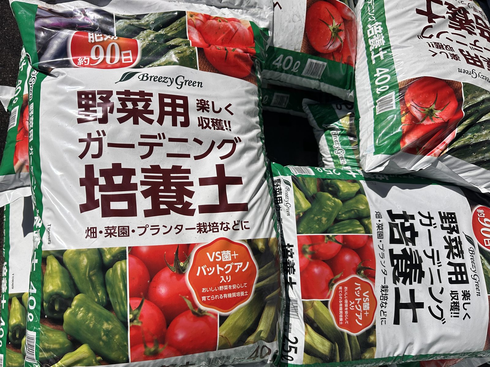 コメリの店頭に積まれた Breezy Green 野菜用ガーデニング培養土の40Lと25Lの袋。袋の表の赤い丸に「肥効 約90日」、「VS菌＋バットグアノ入り」とある